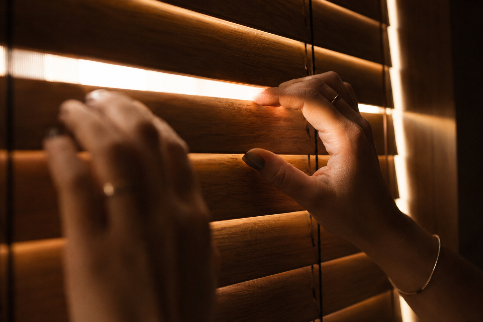 Mãos fechando veneziana de madeira com luz quente escapando pela fresta, simbolizando proteção e segurança